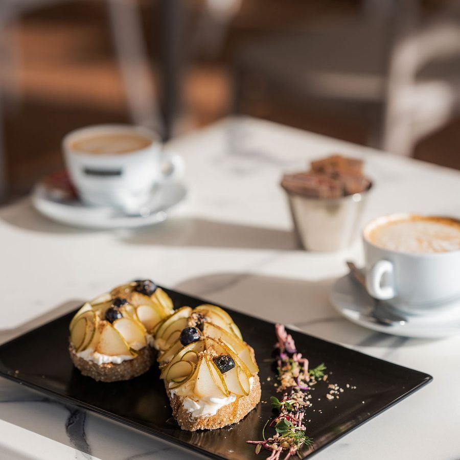 Pear, goat cheese and blueberries on toasted sourdough, with two coffees behind.